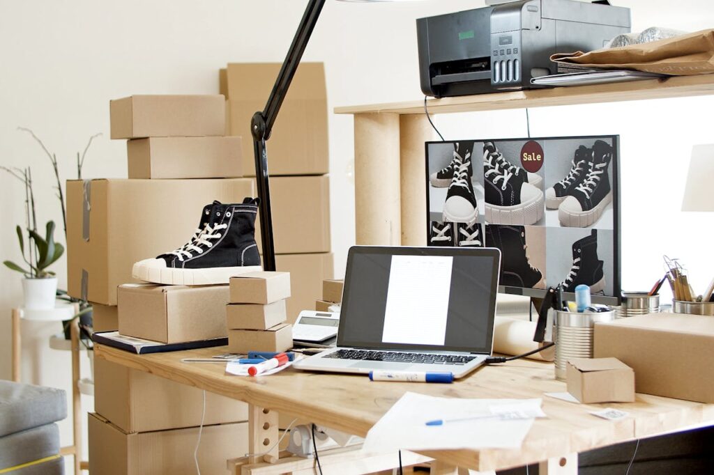 A busy workspace with sneakers, boxes, and a laptop indicating an online shoe store or e-commerce setup.