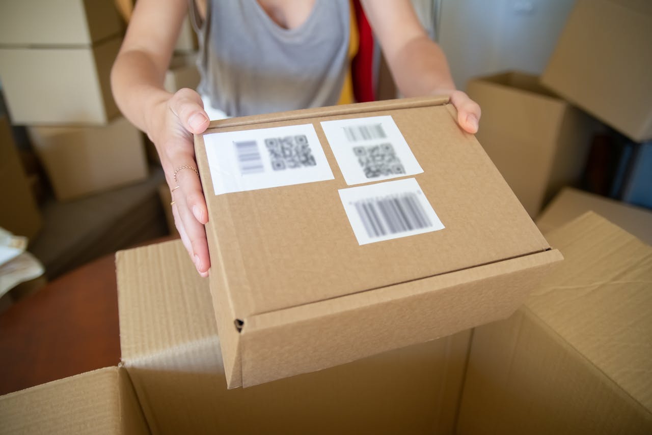 Close-up of a person holding a cardboard box with barcode labels, indoors setting.